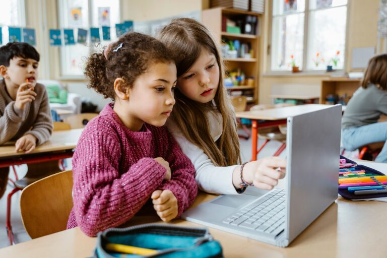 Schoolgirls Sharing Laptop Together At Desk In Classroom